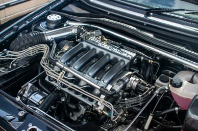Detailní pohled na motorový prostor automobilu s viditelným motorem a různými komponenty.