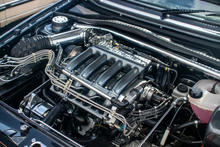 Detailní pohled na motorový prostor automobilu s viditelným motorem a různými komponenty.