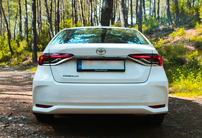 Zadní část bílého vozu Toyota Corolla v přírodě, pro který náš autoservis nabízí kompletní údržbu a servis, včetně diagnostiky parkovacích senzorů.