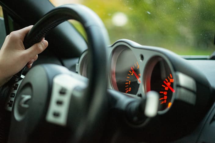 Detail volantu osobního vozu při jízdě rovně po asfaltové silnici — symbol vychýleného volantu a problémů s geometrií kol.