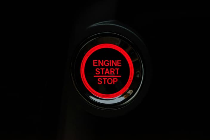 Detailní záběr na červeně svítící tlačítko startování motoru s nápisem ENGINE START STOP na tmavém pozadí.