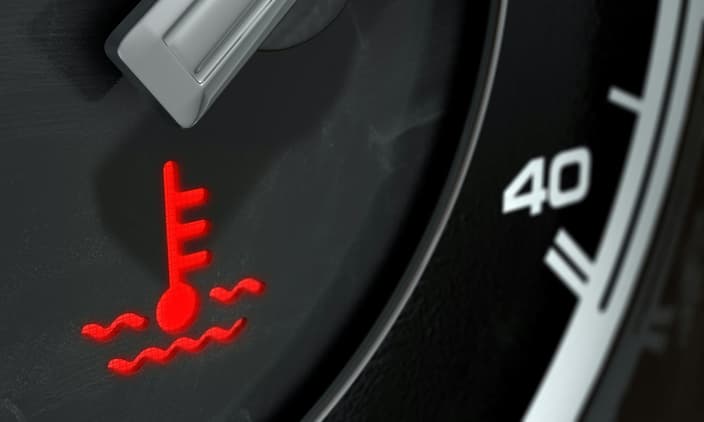 Detail palubní desky automobilu, kde svítí červená varovná kontrolka teploty chladicí kapaliny, což signalizuje přehřívání motoru.