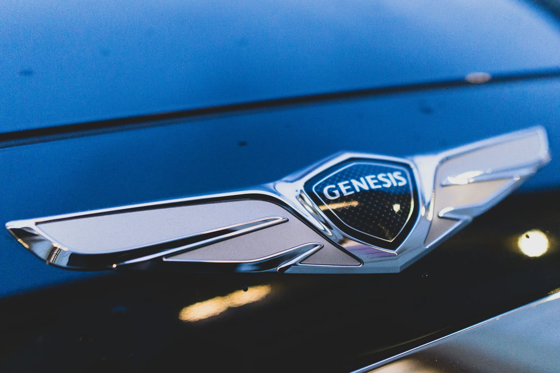 Логотип бренда Genesis на капоте роскошного автомобиля, означающий нашу приверженность предоставлению премиального обслуживания для автомобилей высшего класса.