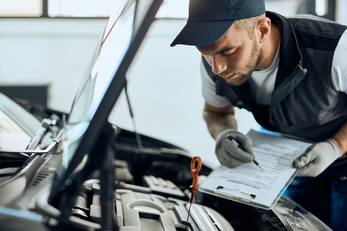 Automechanik provádí předprodejní kontrolu vozu na zvedáku a zapisuje technický stav do protokolu o stavu vozidla.