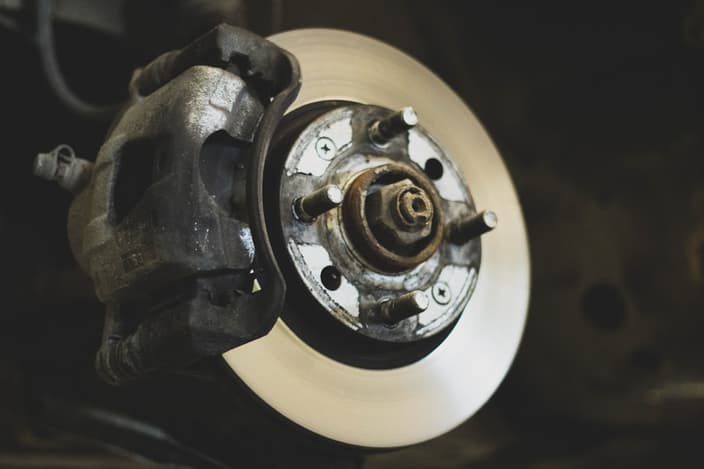 Mechanik v servisu naslouchá zvuku podvozku vozu na zvedáku během diagnostiky neobvyklého hluku.