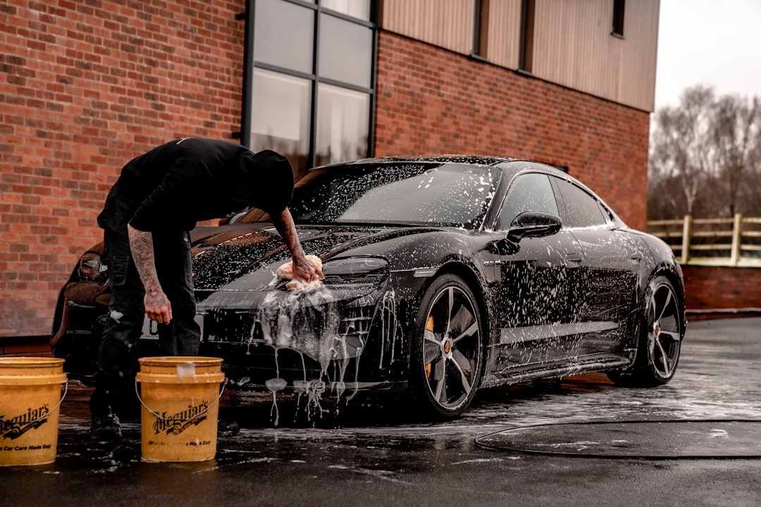 Muž myje tmavé auto pěnou před focením do inzerátu — důkladný úklid je první krok přípravy vozu na prodej.
