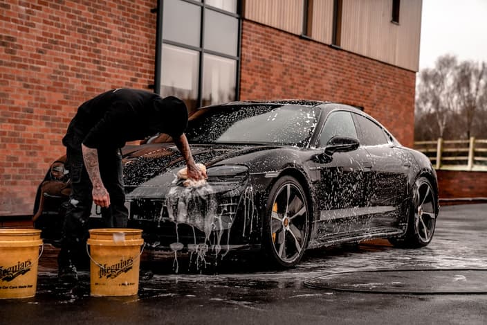 Muž myje tmavé auto pěnou před focením do inzerátu — důkladný úklid je první krok přípravy vozu na prodej.