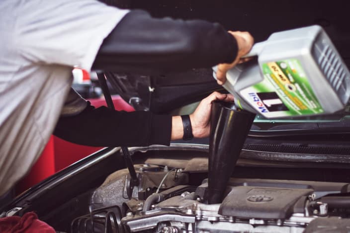 Automechanik provádí profesionální výměnu oleje a doplňuje nový motorový olej do motoru vozidla v autoservisu.