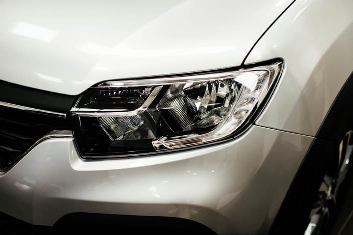 Detailní záběr na čistý a vyleštěný přední světlomet bílého moderního automobilu.