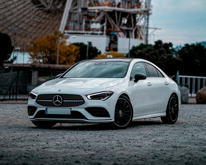 Bílé auto značky Mercedes-Benz zaparkované před průmyslovou budovou.