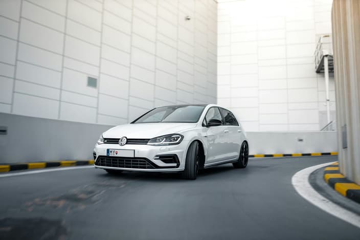 Volkswagen Golf R Mk7 facelift v pohybu na rampě moderního parkovacího domu s černými koly a panoramatickou střechou.