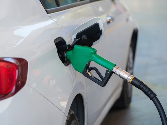 Zelená tankovací pistole zasunutá v nádrži bílého osobního automobilu na čerpací stanici.