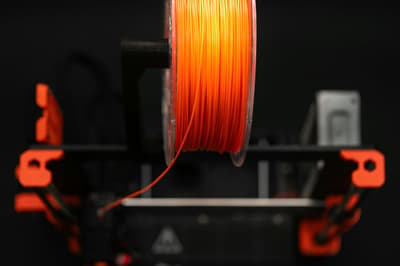Orange 3D printing filament wound on a spool, ready for use in a 3D printer, with focus on the material itself.