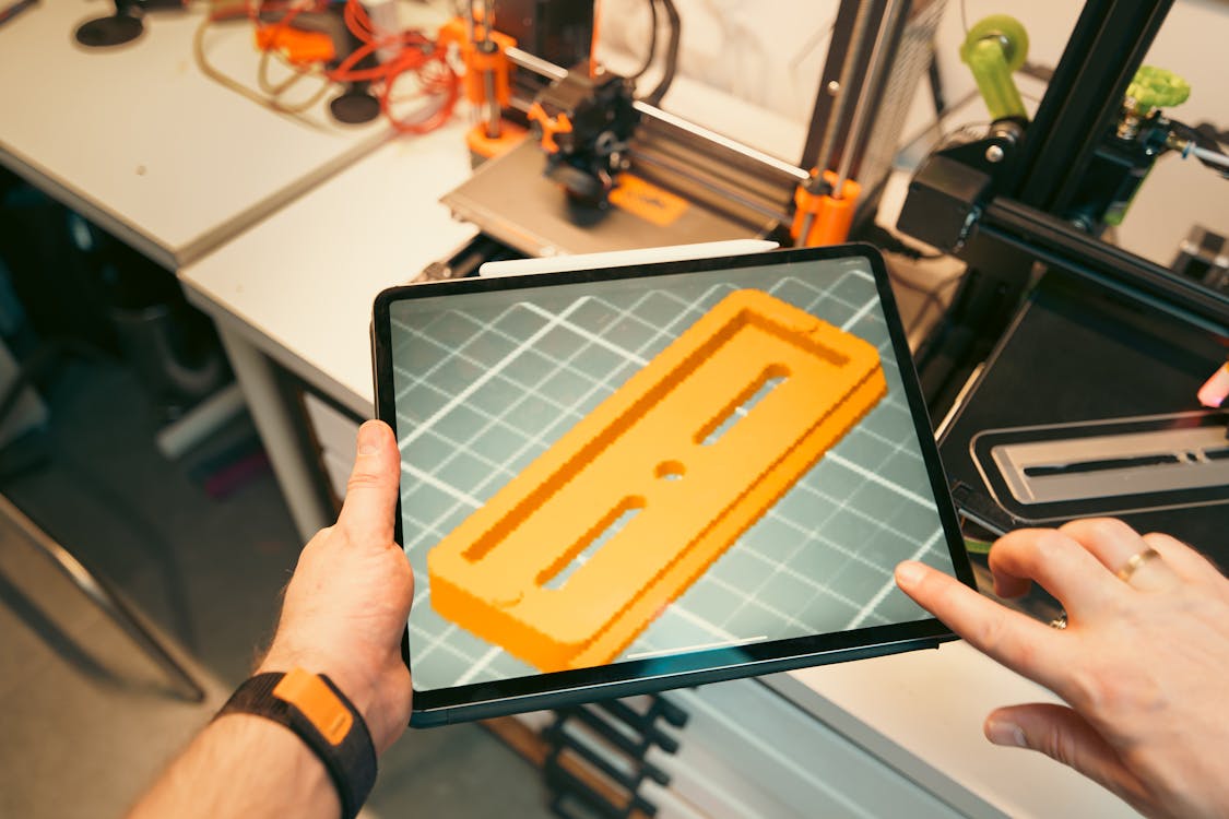 Inženýr kontroluje 3D tištěný prototyp na tabletu v dílně a prohlíží si digitální model souboru před tiskem.