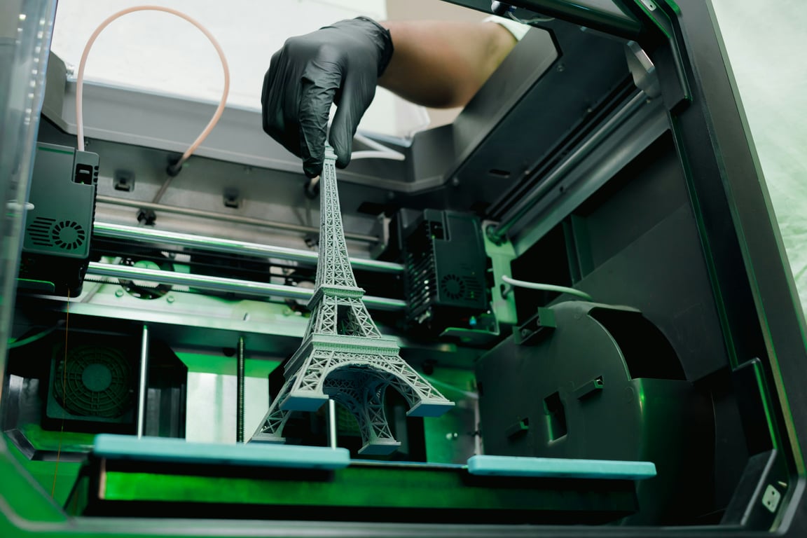 Detailní 3D model Eiffelovy věže vytištěný na profesionální 3D tiskárně v ochranné rukavici.